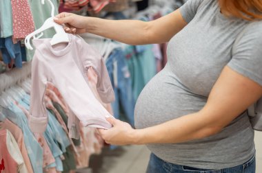 Kafkasyalı hamile kadın bebek kıyafetlerini dükkandan seçiyor. Üçüncü üç aylık dönemin yüzü olmayan hamile annesi.