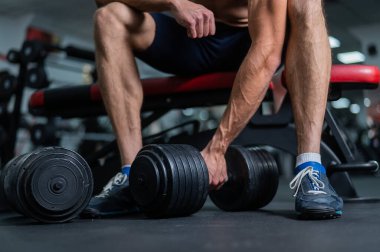 Yüzsüz bir adam bankta oturuyor ve dambılı kaldırıyor.