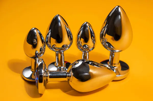 Three size steel butt plugs on an orange background