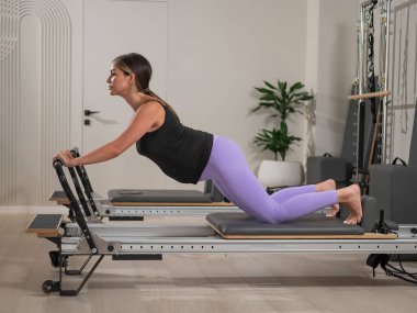 Hamile bir kadın yenilikçi bir makinede kalas kullanıyor. Perinatal yoga.