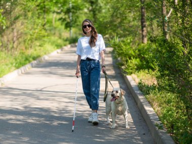 Kör kadın parkta rehber köpekle yürüyor.