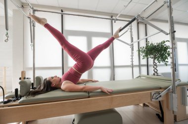 Kadın Cadillac reformatör makinesi üzerinde pilates egzersizi yapıyor.