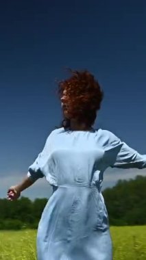 Mavi elbiseli beyaz bir kadın tarlada dans ediyor. Video 360 derece. Dikey video