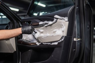 Bir adam arabanın içini köpük ve fırçayla temizler. Kapıyı temizleyin.