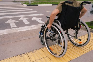 Tekerlekli sandalyedeki yaşlı bir kadının yaya geçidine gidişinin arka görüntüsü. Tekerlekler üzerinde yakın plan