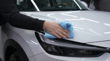 Bir tamirci mikrofiber bezle beyaz bir arabanın vücudunu siler.