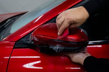 Usta bir arabanın dikiz aynasına vinil film uyguluyor.