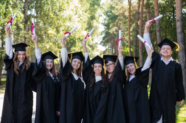 Mezuniyet elbisesi giymiş, açık havada diplomalarını gösteren bir sürü genç öğrenci.