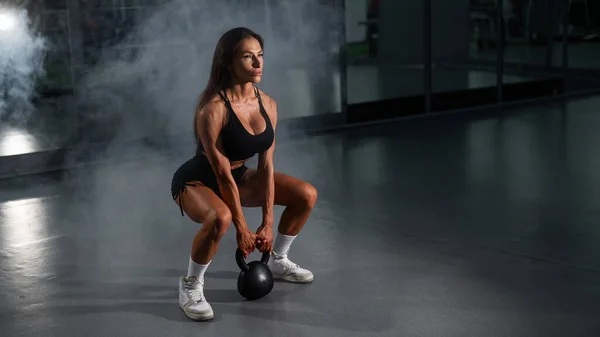 Caucasian woman squats with kettlebell in the gym