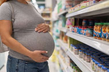 Meçhul hamile kadın marketten bebek maması seçiyor. Sebze püresi dolu kavanozlar