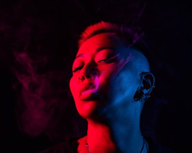 Kısa saçlı, neon ışıkta sigara içen Asyalı kadının yakın portresi.