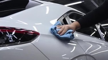 Bir tamirci mikrofiber bezle beyaz bir arabanın vücudunu siler.