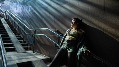 Merdivenlerin yanındaki metroda poz veren Asyalı genç bir kadının portresi.