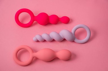 Pembe arka planda çeşitli şekil ve boyutlarda üç adet silikon anal boncuk.