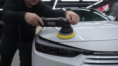 Bir tamirci beyaz bir arabanın kaputunu cilalar. Vücut onarımı