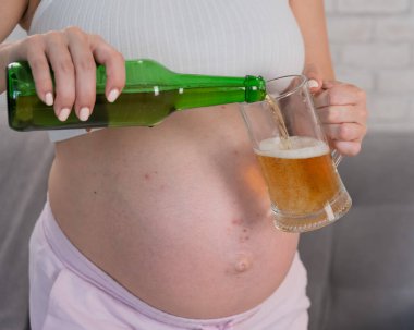 Suratsız hamile kadın bardağa bira dolduruyor.