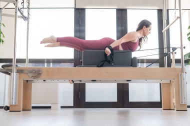 Kadın Cadillac reformatör makinesi üzerinde pilates egzersizi yapıyor.