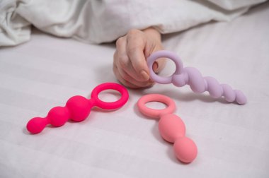 Bir kadın yatakta yatarken bir setten anal boncuk seçer.