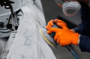 Bir tamirci, bir araba gövdesindeki macunu makineyle kumlar. Bir kazadan sonra onarım