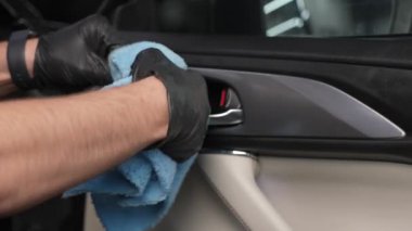 Bir adam arabanın içini mikrofiber bir bezle siliyor.