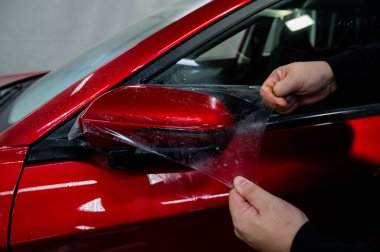Usta bir arabanın dikiz aynasına vinil film uyguluyor.