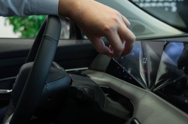 Bir adam yeni bir arabanın ön panelinden koruyucu filmi çıkarır.