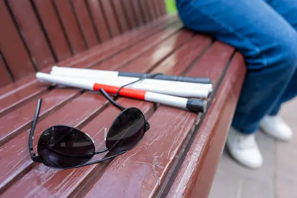 Sunglasses and a folding cane for the blind on a bench