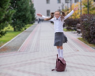 Üniformalı ve sırt çantalı mutlu beyaz kız okuldan sonra dışarı atlıyor.