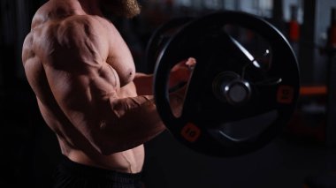 Yüzsüz üstsüz bir adam spor salonunda halterle egzersiz yapıyor. Ağırlıklarla bibik bukleler