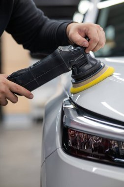 Yörüngesel cilalama makinesi kullanılarak beyaz arabanın kaput yüzeyinin parlatılması işlemi. Dikey fotoğraf