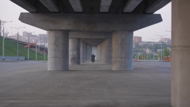 一个穿着夹克和头盔的男人在桥下骑电动摩托车 — 图库视频影像
