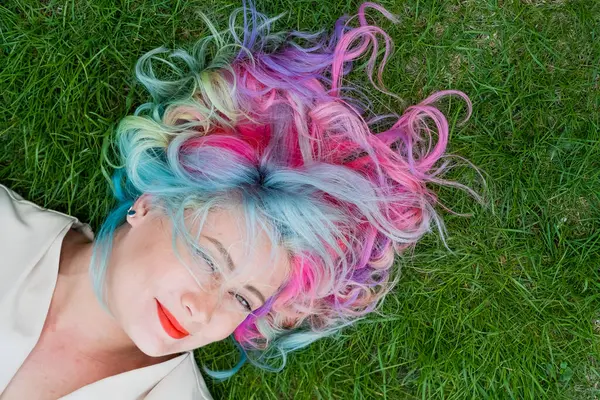 Kafkasyalı kadının yeşil çimlerin üzerinde uzanan çok renkli saçları var.