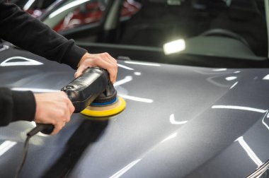 Bir tamirci gri bir arabanın kaputunu cilalar.