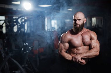 Tişörtsüz poz veren kaslı kel adam. Vücut geliştirici spor salonunda vücudunu gösteriyor.