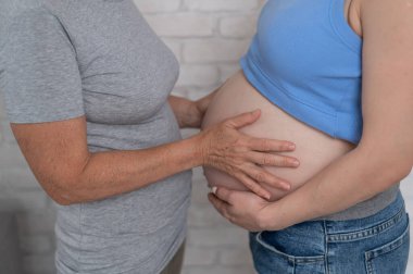 Yaşlı bir kadın hamile kızının karnına dokunur. Yakın plan.