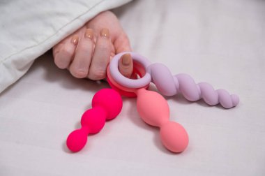 Yatakta yatarken elinde üç farklı anal boncuk tutan kadın.