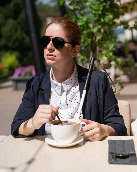 Blind woman in business suit drinking coffee in outdoor cafe