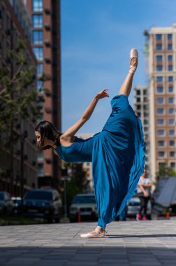 Açık havada poz veren mavi elbiseli güzel bir Asyalı balerin. Şehir manzarası. Dikey fotoğraf