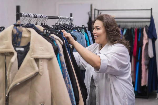 A fat woman in a plus size store chooses clothes while sorting through hangers