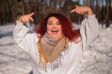 A chubby red-haired woman in a white sweatshirt. Girl fooling around in the park in winter