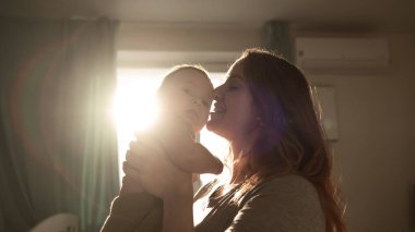 Kafkasyalı bir kadın yeni doğan oğlunu güneş ışığında şefkatle öper.