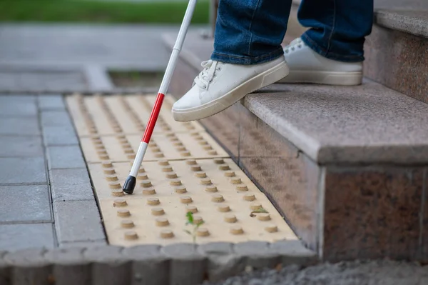 Close-up of female foot, walking stick and tactile tiles. Blind woman walking down stairs using a cane