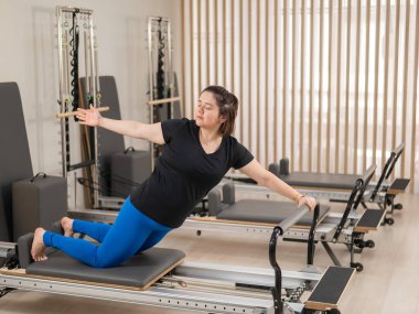 Aşırı kilolu beyaz kadın bir reformcu üzerinde pilates egzersizi yapıyor.