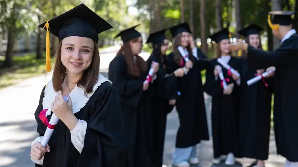 Group of happy students in graduation gowns outdoors. A young girl is happy to receive her diploma