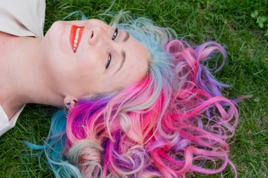 Kafkasyalı kadının yeşil çimlerin üzerinde uzanan çok renkli saçları var.