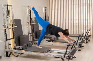 Aşırı kilolu beyaz kadın bir reformcu üzerinde pilates egzersizi yapıyor.
