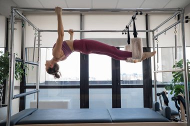 Kafkasyalı bir kadın, reformcu bir simülatörde pilates yapıyor. Asılma konumu