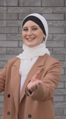 Mavi gözlü genç bir kadının portresi gri tuğla bir duvara karşı tesettürlü. Dikey video
