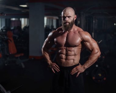 Tişörtsüz poz veren kaslı kel adam. Vücut geliştirici spor salonunda vücudunu gösteriyor.