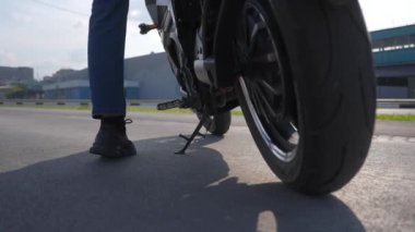 Adamın biri elektrikli motosiklete biniyor, amuda kalkıyor ve uzaklaşıyor.